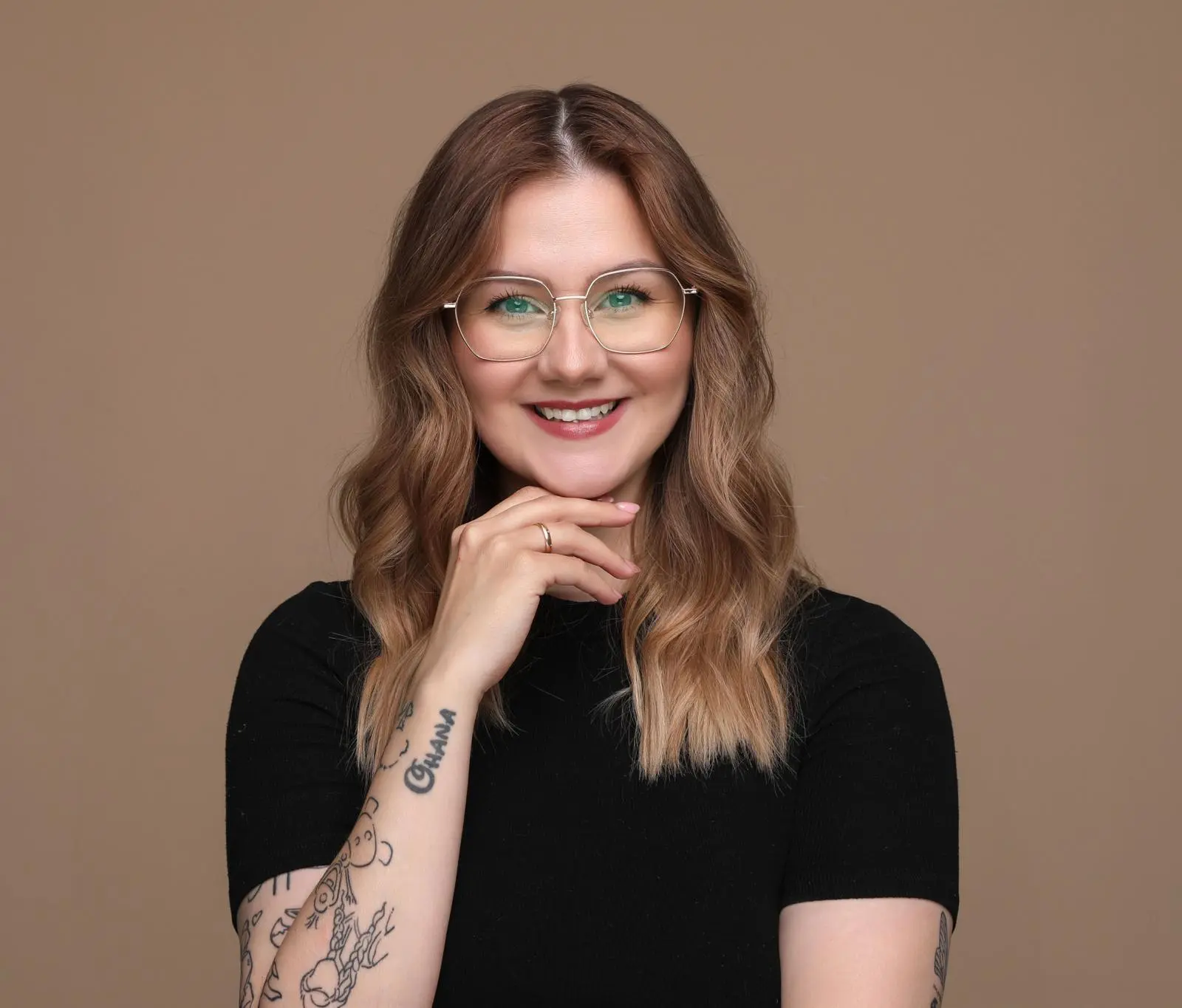 Mitarbeiterin Jessica. Freundliches Lächeln, schwarzes T-Shirt. Langes hellbraunes Haar. Tätowierung auf dem rechten Arm.