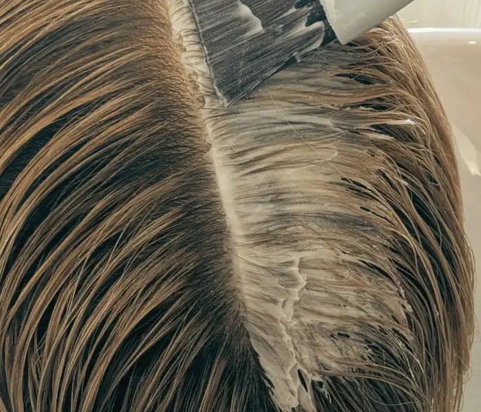 Eine Haarmaske wird mit einem Pinsel auf den Kopfansatz aufgetragen