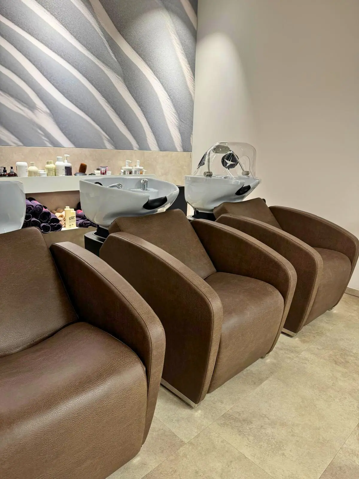 Drei braune Massagesessel nebeneinander. Am Kopfende sind Kopfwaschbecken. An einem Waschbecken befindet sich eine Headspa Haube